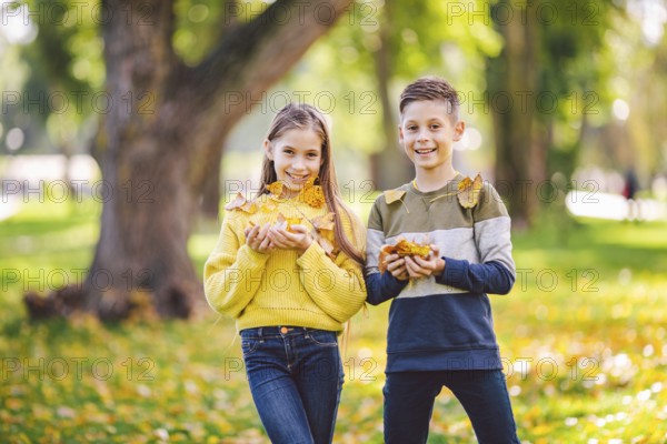 Friendship between siblings. Siblings together outside with bright coloured background. Kids autumn portrait. Brother and sister playing in autumn park leaves. Family active fall weekend concept