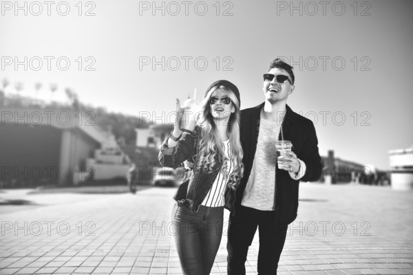 Smiling couple walk at the street in weekend and drink some cocktails