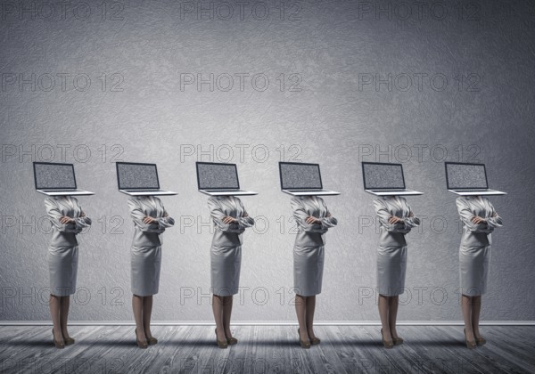 Business women in suits with laptop instead of their heads keeping arms crossed while standing in a row in empty room with gray wall on background