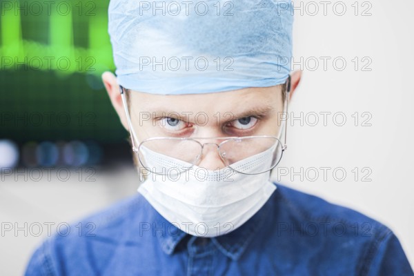 A surgeon with an intense expression, wearing mask and glasses, in a blurred clinical background