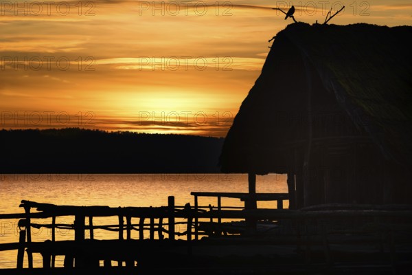 Amazing sunset landscape with a shadowed wooden hut and a bird on top of it, on a lake, at golden hour, at Bodensee lake, Germany, Europe