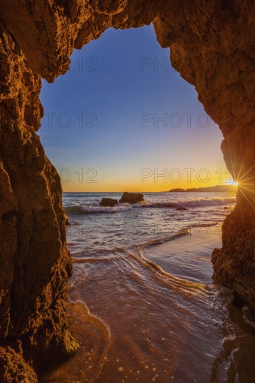 View from the beach through a rock formation to the Atlantic Ocean, sunset on the Algarve coast, Portugal, Europe