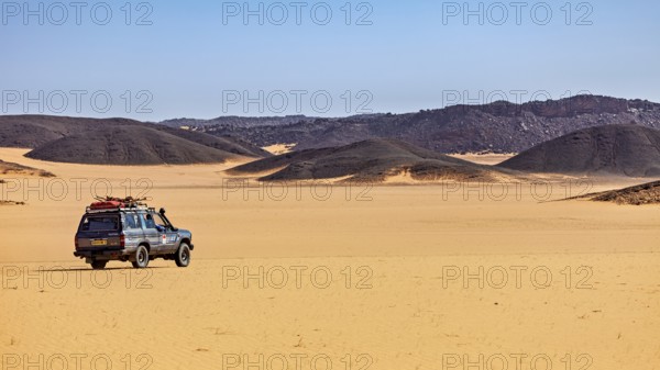 An off-road vehicle stands in vast sand dunes under a clear, sunny sky, off-road through the landscapes of the Sahara in Algeria