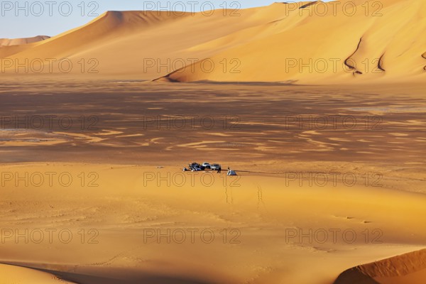 Wide sand dune landscape in yellow tones, with a small camp in the middle of the dunes, tent camp in the endless sand and dune landscape in the Sahara in Algeria