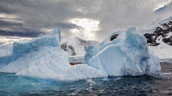 Large icebergs in a cloudy sky with an opening in the background that lets sunlight through, icebergs in the landscape of the Southern Ocean in Antarctica