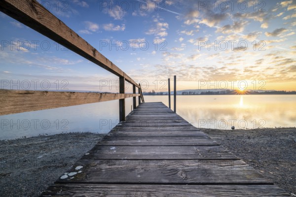 A wooden footbridge leading onto a calm lake as the sun sets under a cloudy sky, Naturfreundehaus, Markelfingen, Untersee, Lake Constance, Baden-Württemberg, Germany, Europe