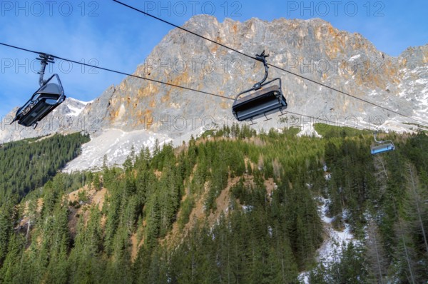 Alpine scenery with the rocky peaks of the Alps mountains and ski lifts rolling on a cableway over the snowy fir forests, in Ehrwald, Austria, Europe