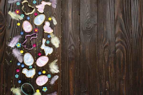Sugar sprinkles, candies, feathers, cookie cutters, Easter frosted cookies in shape of egg chicken and rabbit on wooden table background. Flat lay mockup with copy space