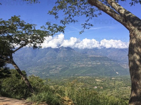 Tree framed view into a green valley and mountains with white clouds and blue sky, Barichara, Colombia, South America