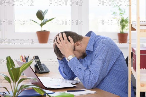 Office employee clutching his head in his hands while reading a document