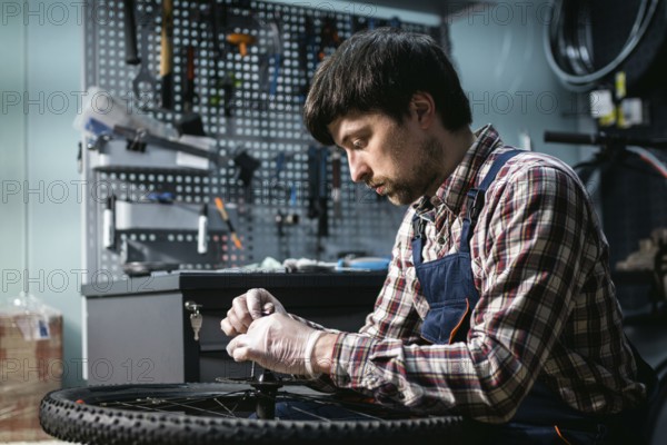 Young caucasian repairman repairing mountain bike wheel in bike shop workshop. Fixing bicycle. Caring for you wheels. man mechanic working in garage. Worker fixing cycle gear. Small business theme