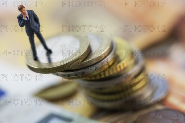 Figure of a thoughtful businessman between euro coins, studio shot, Germany, Europe