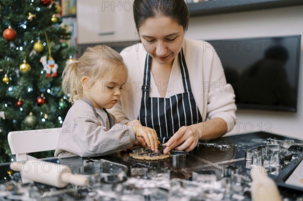 Mom puts cookie cutters on the dough next to the little girl pressing them.