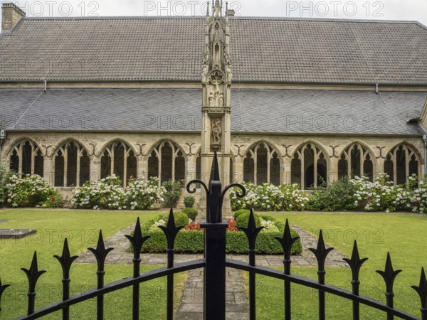 A well-kept courtyard with Gothic architecture, flower beds and a decorative fence in the foreground, xanten, lower rhine, germany