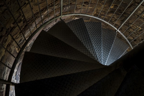 Steps of old metal spiral staircase disappear in darkness