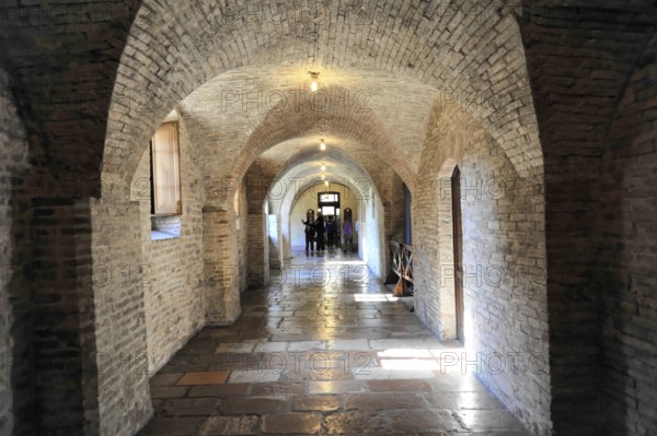 Basilica Santa Maria degli Angeli, Assisi, Umbria, Italy, A long vaulted corridor with brick walls and stone floor, dimly lit, leads into the distance, Assisi, Umbria, Italy, Europe