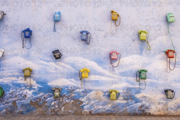 Colored telephones hanging in a blue and white wall. Urban art in the middle of nowhere