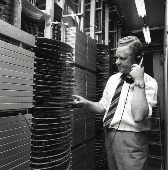 Telephony in the 1970s. A man in a room with an automatic switchboard connecting the calls through a mechanical device that connected the calling and receiving parts. The manufacturer is LM Ericsson. Sweden 1971 Kristoffersson ref ED