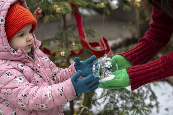 Crystal christmas ball with house and snow inside. Hands with green gloves gives transparent ball to a child