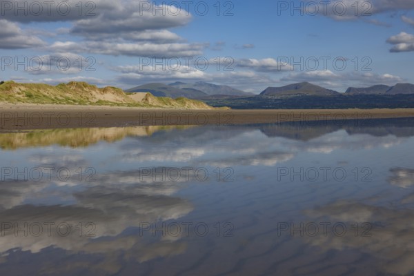 Reflection of clouds and mountains of Snowdonia National Park in the water on the beach, Newborough, Anglesey, Wales, Great Britain