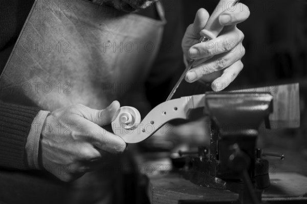Craftsman sculpting a wooden spiral detail on a violin scroll with a chisel