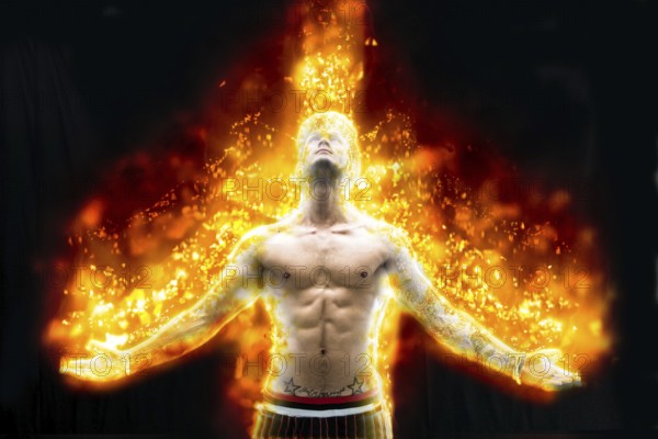 Tattooed muscular man with nude torso holding hands apart and burning in fire on black background