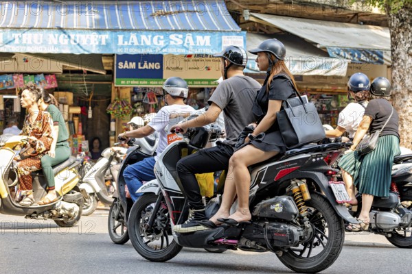 People ride scooters through a busy city shopping street during the day, people on scooters ride through the streets of Hanoi Vietnam
