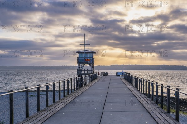 A long jetty with a tower leading into the sea under a dramatically cloudy sky with rays of sunshine, Glücksburg, Germany, Europe