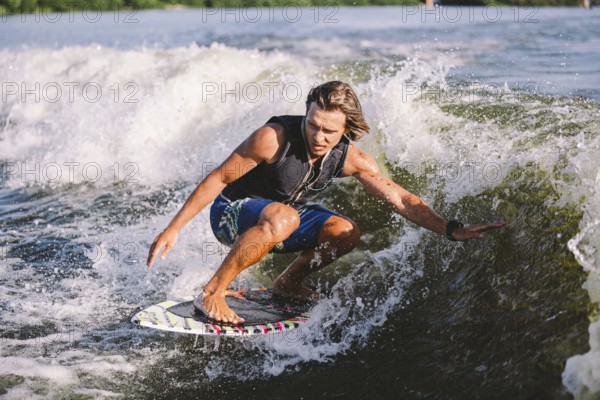 Young athletic man with long hair wakesurfing on waves of river in sunny summer weather. Ttheme outdoor activities in summer. Water sports wakesurf on the board. sliding wakeboarder in water splash