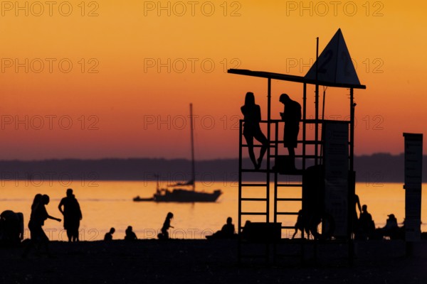 Silhouetted figures against an orange sunset on the beach with a lifeguard tower and a calm Lake Erie as seen from Port Stanley Beach in Ontario, Canada, North America