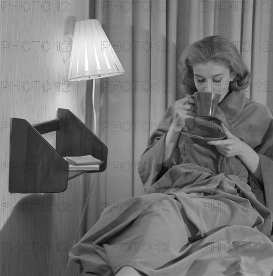 Teatime in the 1950s. A young woman in an evening gown sits comfortably and drinks a cup of tea. Sweden 1950s