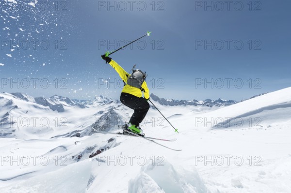 A skier in full sports equipment jumps into the abyss from the top of the glacier against the background of the blue sky and the Caucasian snow-capped mountains. View from the back. Elbrus region. Russia