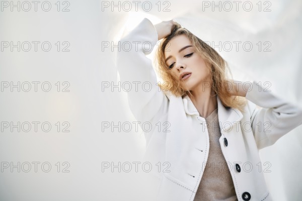 Young attractive woman in white clothes posing on abstract pale background looking at camera confident. Soft sunny colors. Beauty concept