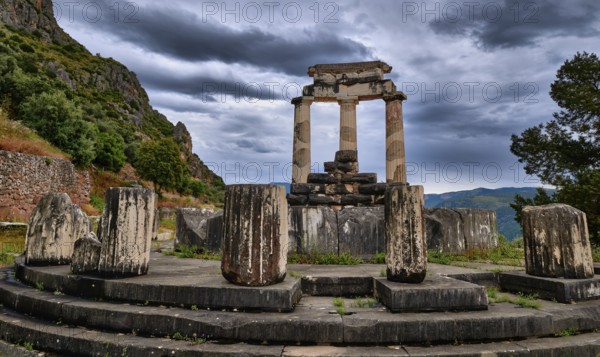 Ruins of Tholos of ancient Greek goddess Athena Pronaia in Delphi, Greece. Three Doric columns with relieves on frieze of circular temple on slope of sacred mount Parnassos and next to famous Delphi complex. UNESCO World heritage site. Rear view