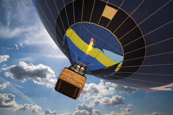 Hot air balloon with gondola in front of a blue sky with white clouds