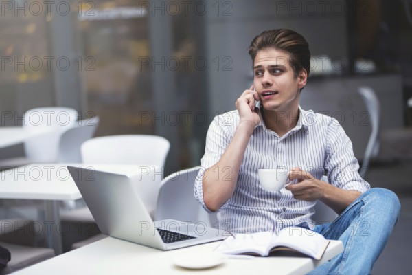 Handsome caucasian young man with phone working on laptop and smiling while enjoying coffee in cafe
