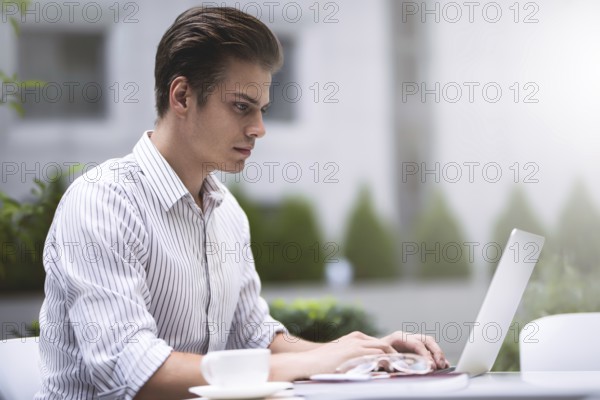 Smart attitude. Positive handsome man using a laptop and sitting in the cafe while surfing the internet