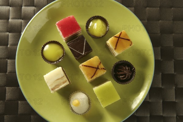 Varied pastries in green dish. Little colorful cakes