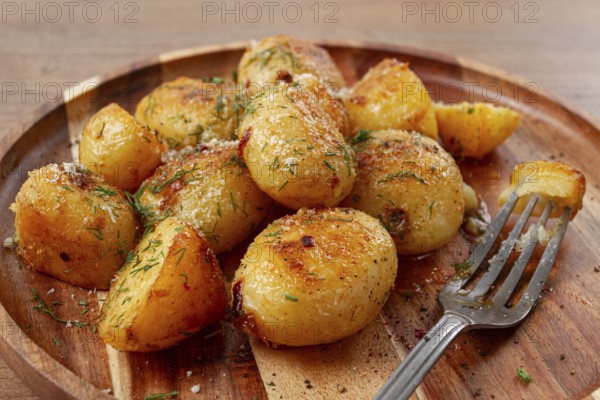 Half-eaten fried new potatoes, with butter and dill, on a wooden plate, with a fork, at home, without strangers