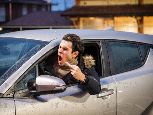 Aggressive man driving car and screaming away while showing obscene gesture on street