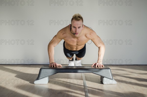 Young aerobics male coach shirtless leaning on step teaching class, looking at camera
