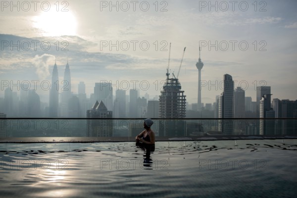 Woman enjoying cityscape of Kuala Lumpur from rooftop swimming pool. Urban scene with skyscrapers, Petronas Tower and Kuala Lumpur Tower, Malaysia, Asia