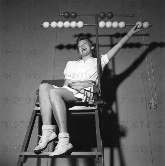 Tennis in the 1940s. A young woman is sitting in the tennis jugdge's chair. The wooden balls in bright and dark on each side are for visually mark won games and sets for each player Sweden 1942 Kristoffersson ref M92-5