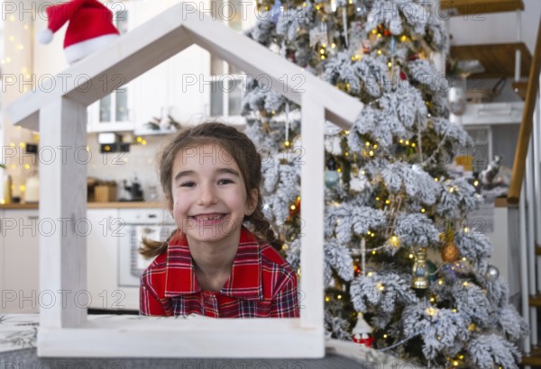 Happy child with tiny house in cozy home with Christmas decor of festive white kitchen. Gift for New Year. Insurance, moving to new house, mortgage, rent and purchase real estate