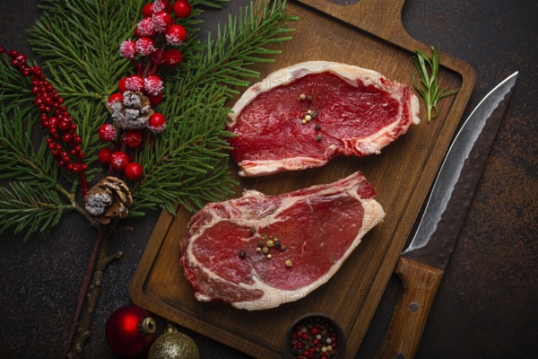 Two raw uncooked meat beef steaks on wooden cutting board with knife and seasonings on dark rustic background with Christmas festive decoration from above, food photography, food photography