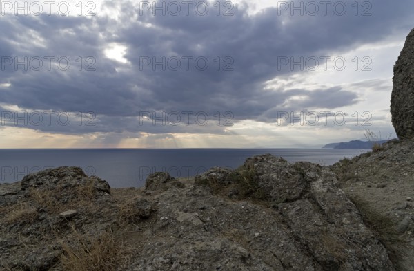 The rays of the sun over the sea make their way through the clouds.Cape Meganom, Crimea, mid-October