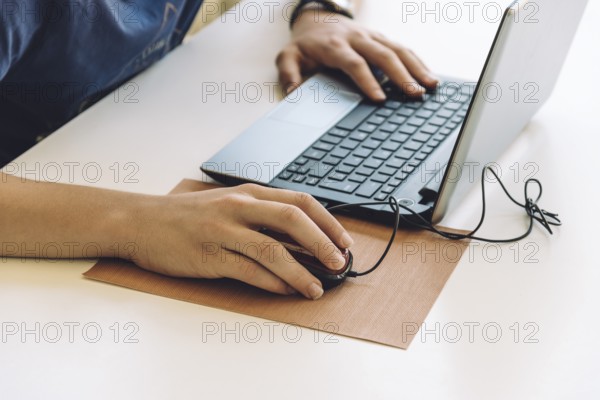 Young man working with laptop, hands on notebook computer and mouse. Blurred background. Student working at home