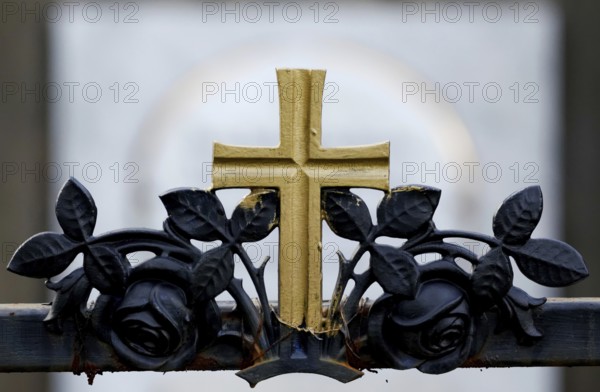Golden cross on a wrought-iron fence of a grave in a cemetery