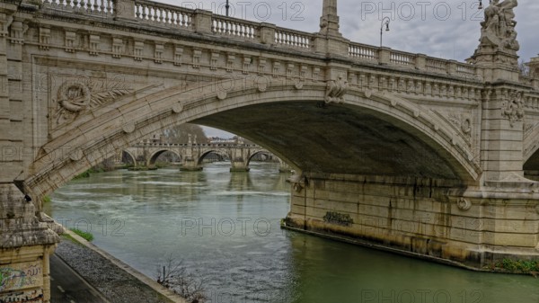 A grand stone bridge with intricate carvings spans over a calm river beneath a cloudy sky, Vittorio Emanuele II bridge, Rome, Lazio, Italy, Europe