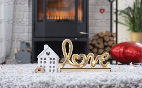 Key to house with keychain against background of fireplace stove with fire and firewood in Valentine decor, love home. Moving to new house, mortgage, rent and purchase real estate